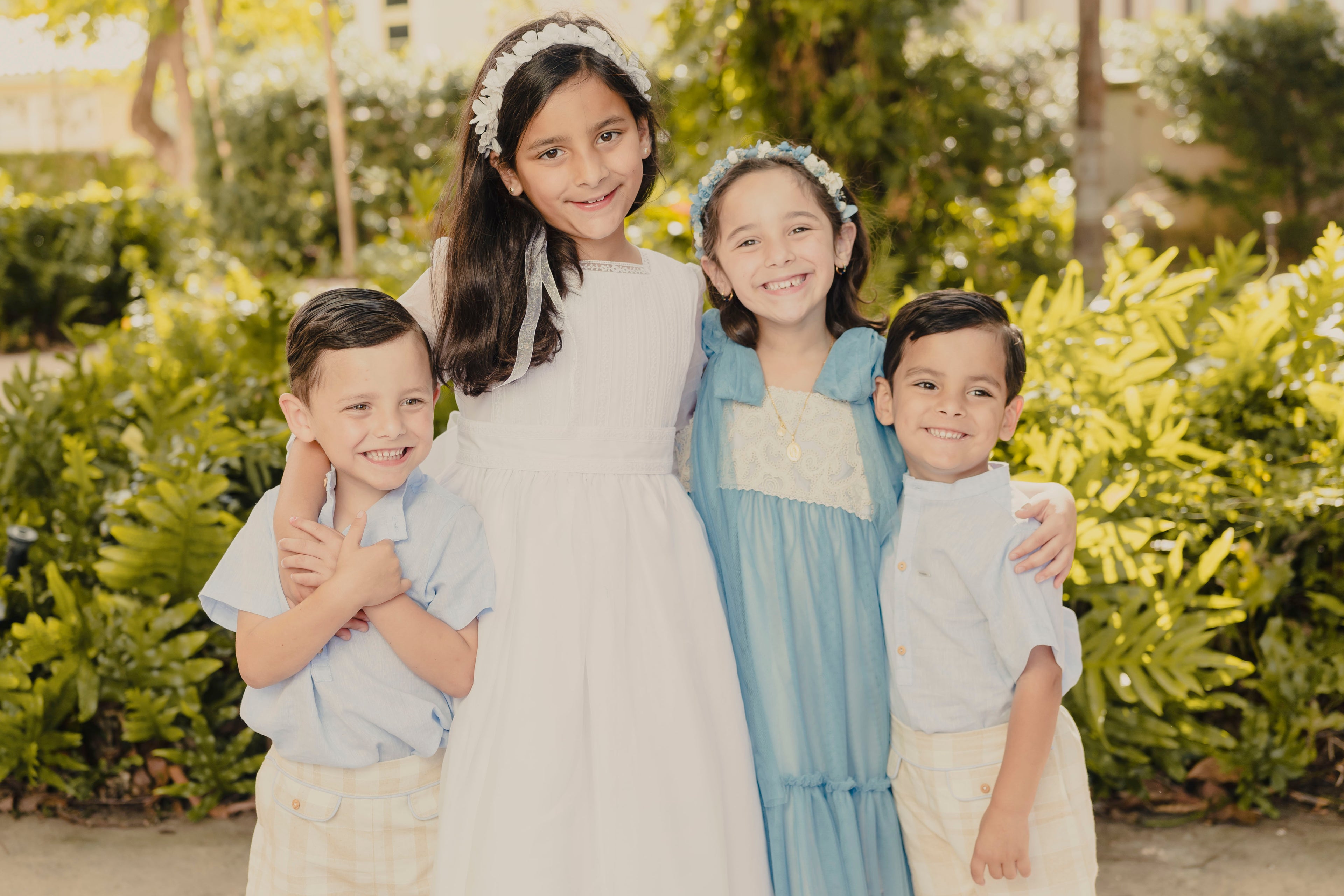 Four children posing together outdoors with greenery in the background